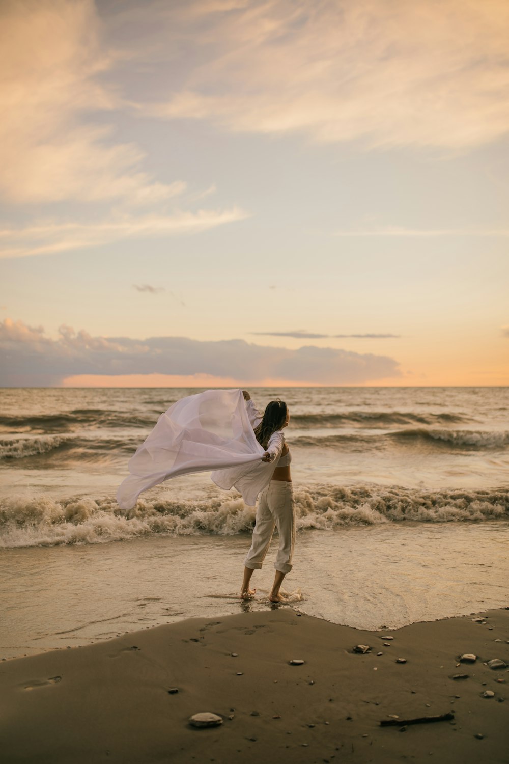 a woman walking on a beach holding a white sheet