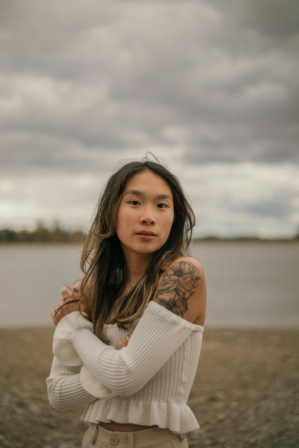 a woman with a tattoo on her arm standing in front of a body of water