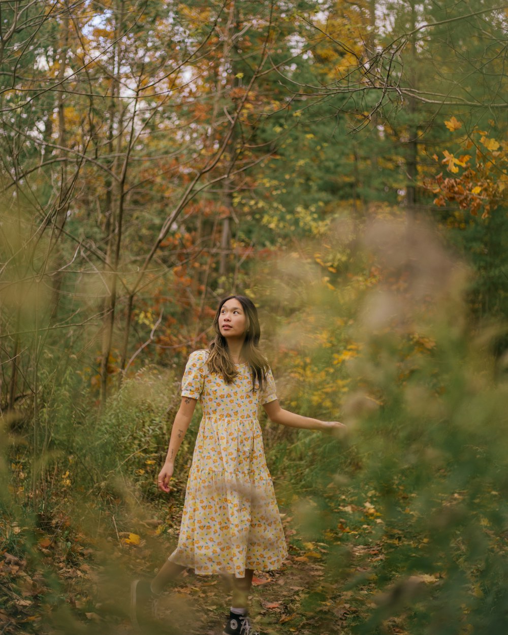 a woman in a yellow dress standing in a forest