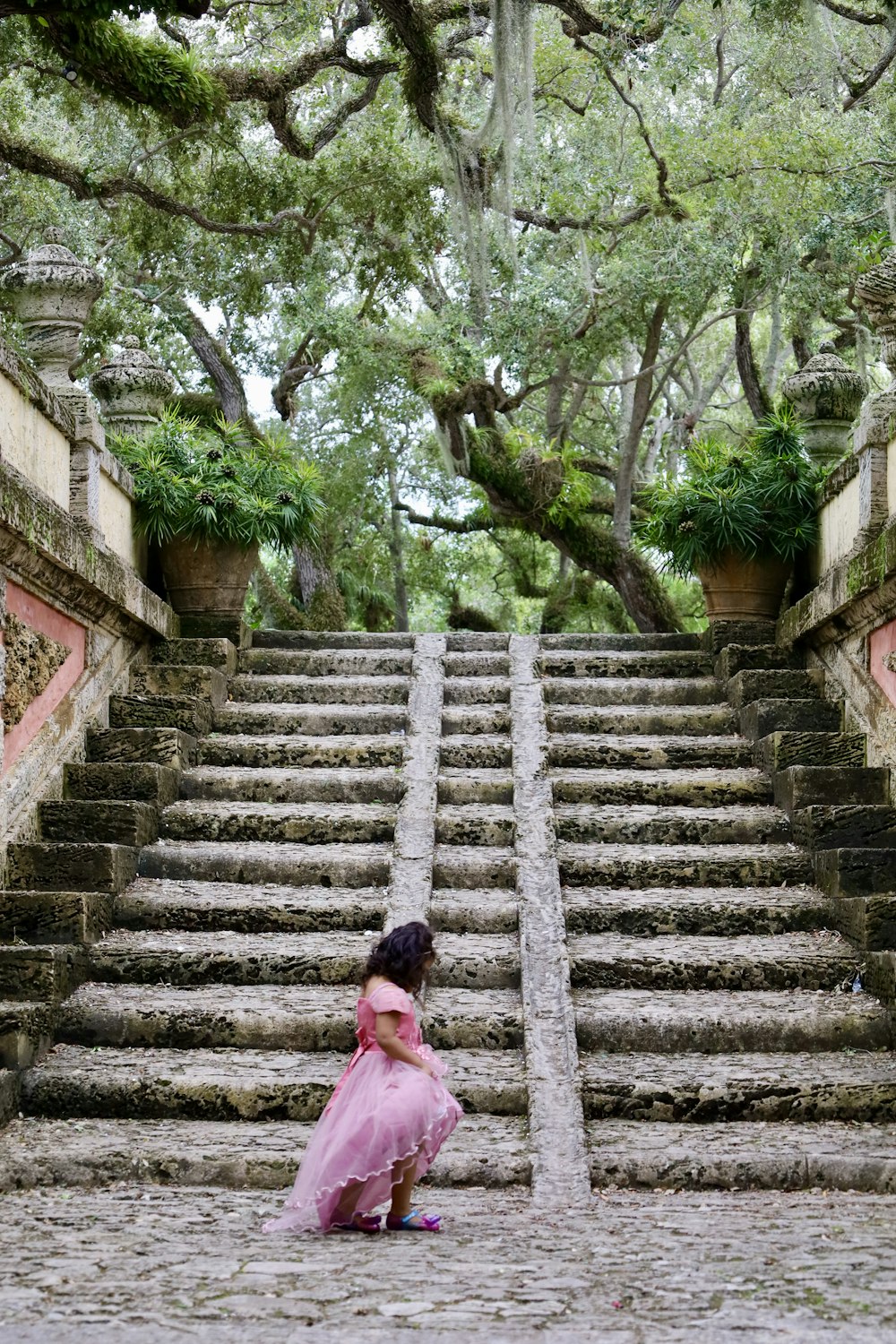a young girl in a pink dress sitting on steps