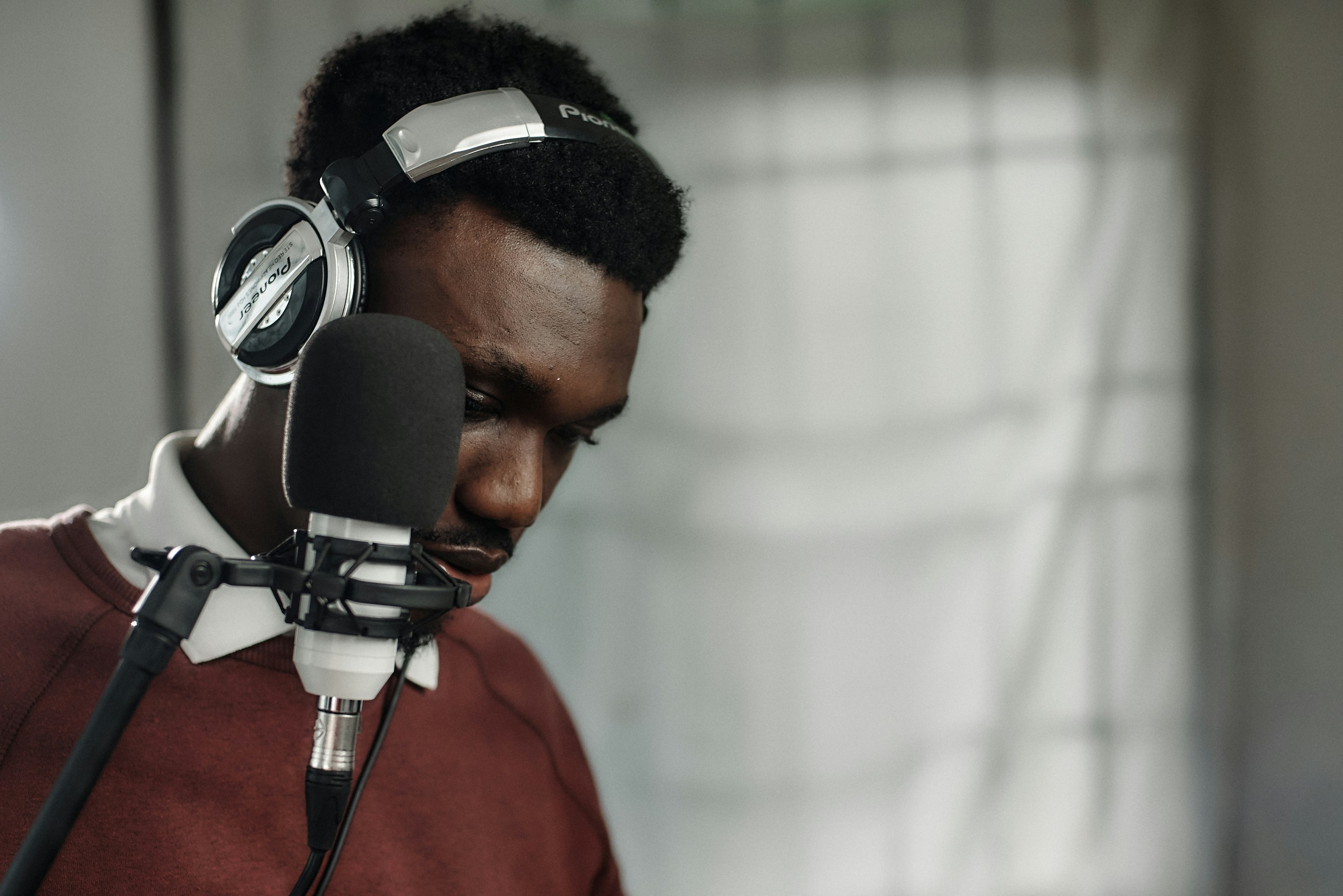 African male voice over artist recording a voice-over script with a condenser and Pioneer exclusive headphones.