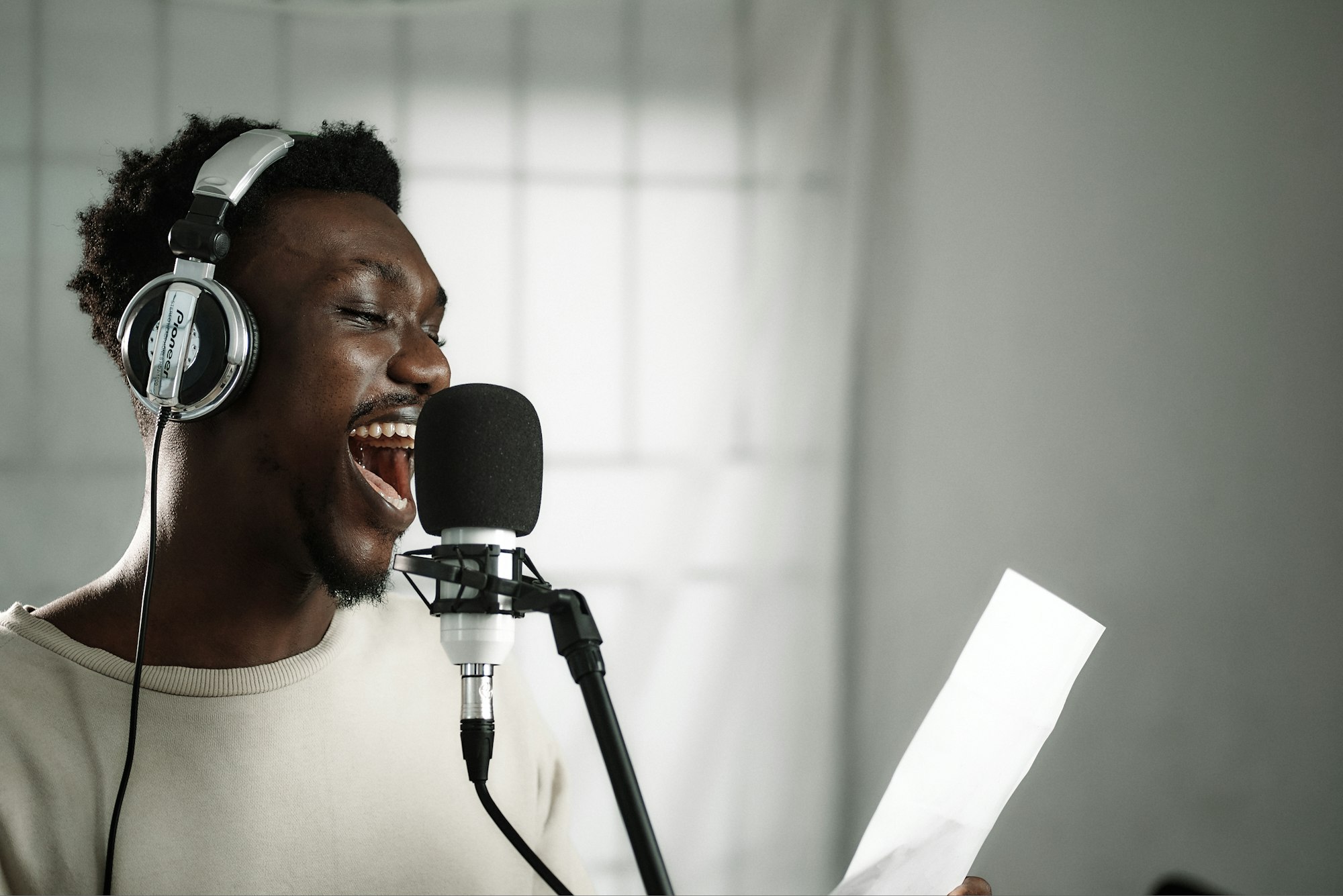 African male voice over artist recording a voice-over script with a condenser and Pioneer exclusive headphones.