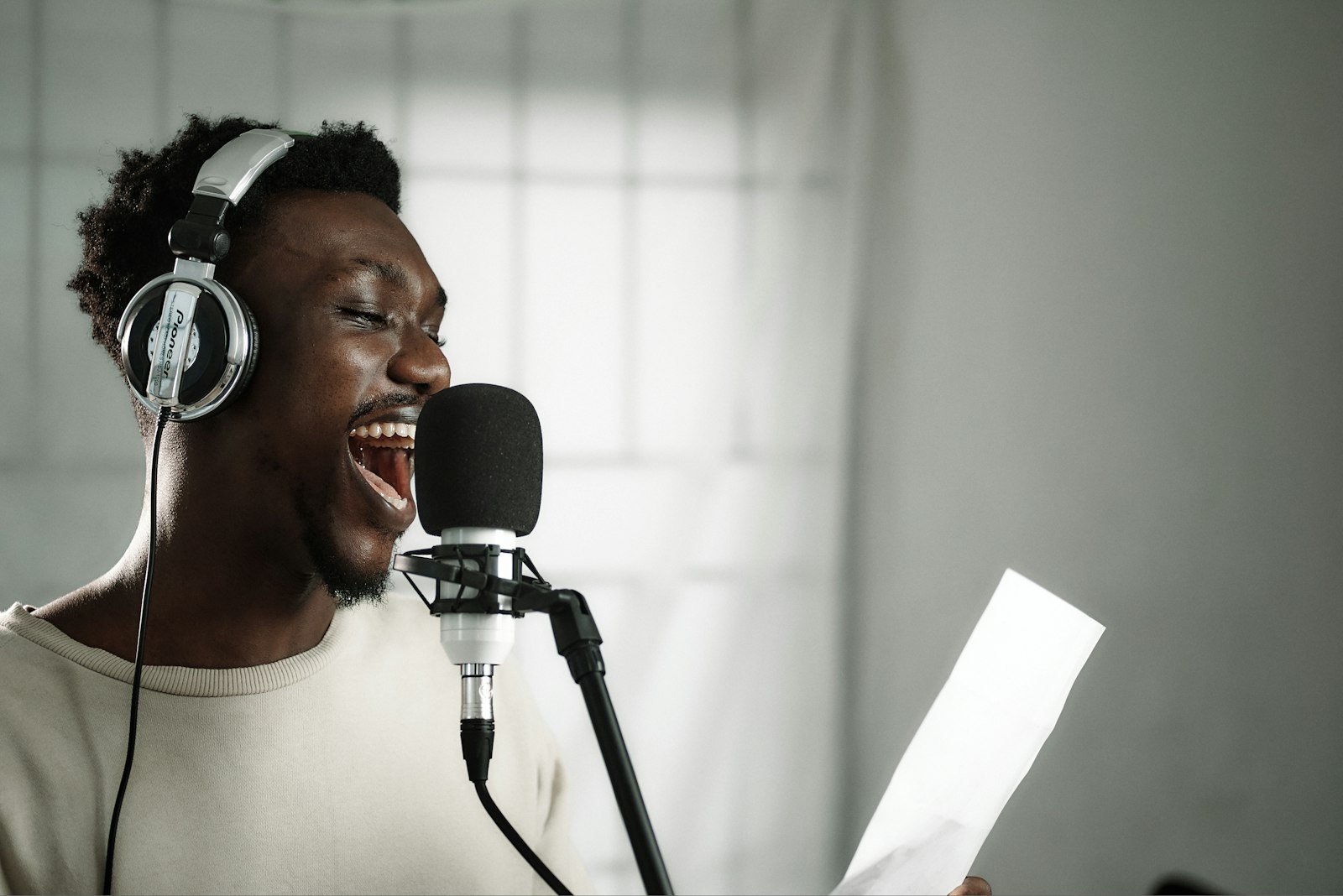 A voice-over artist wearing headphones speaking into a condenser microphone