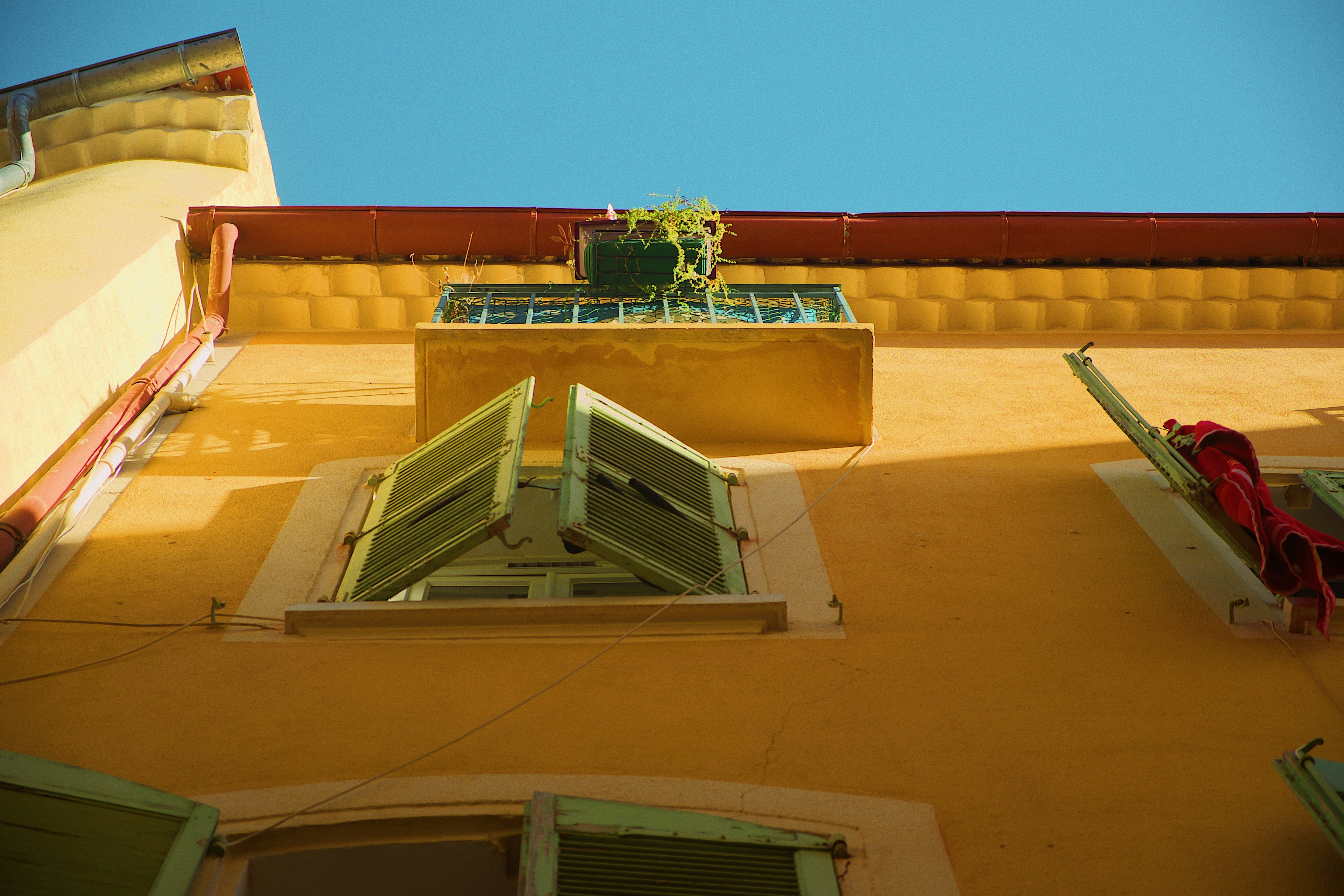 a yellow building with green shutters and a planter
