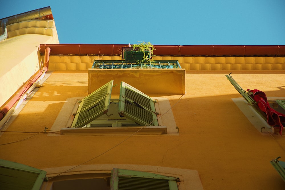 a yellow building with green shutters and a planter