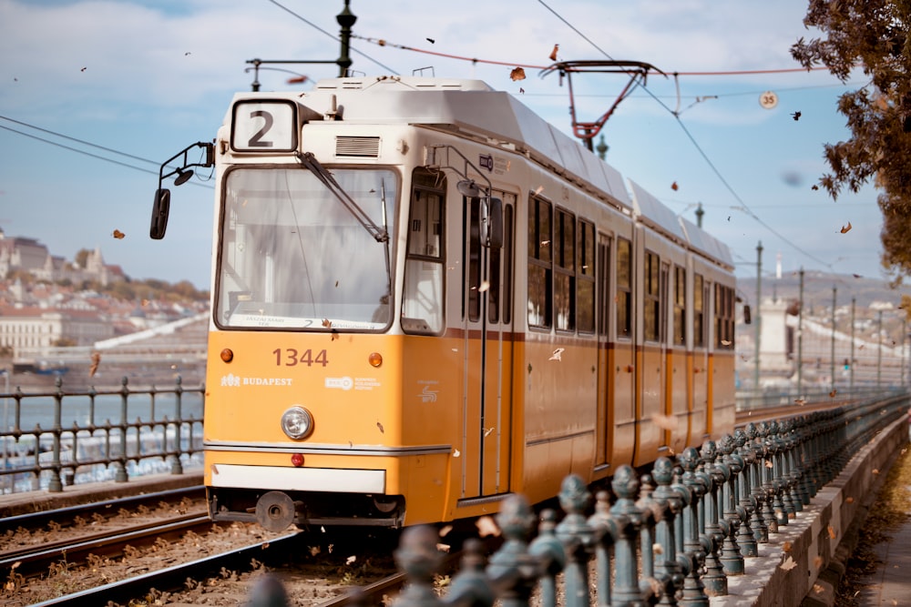 a yellow train traveling down train tracks next to a fence