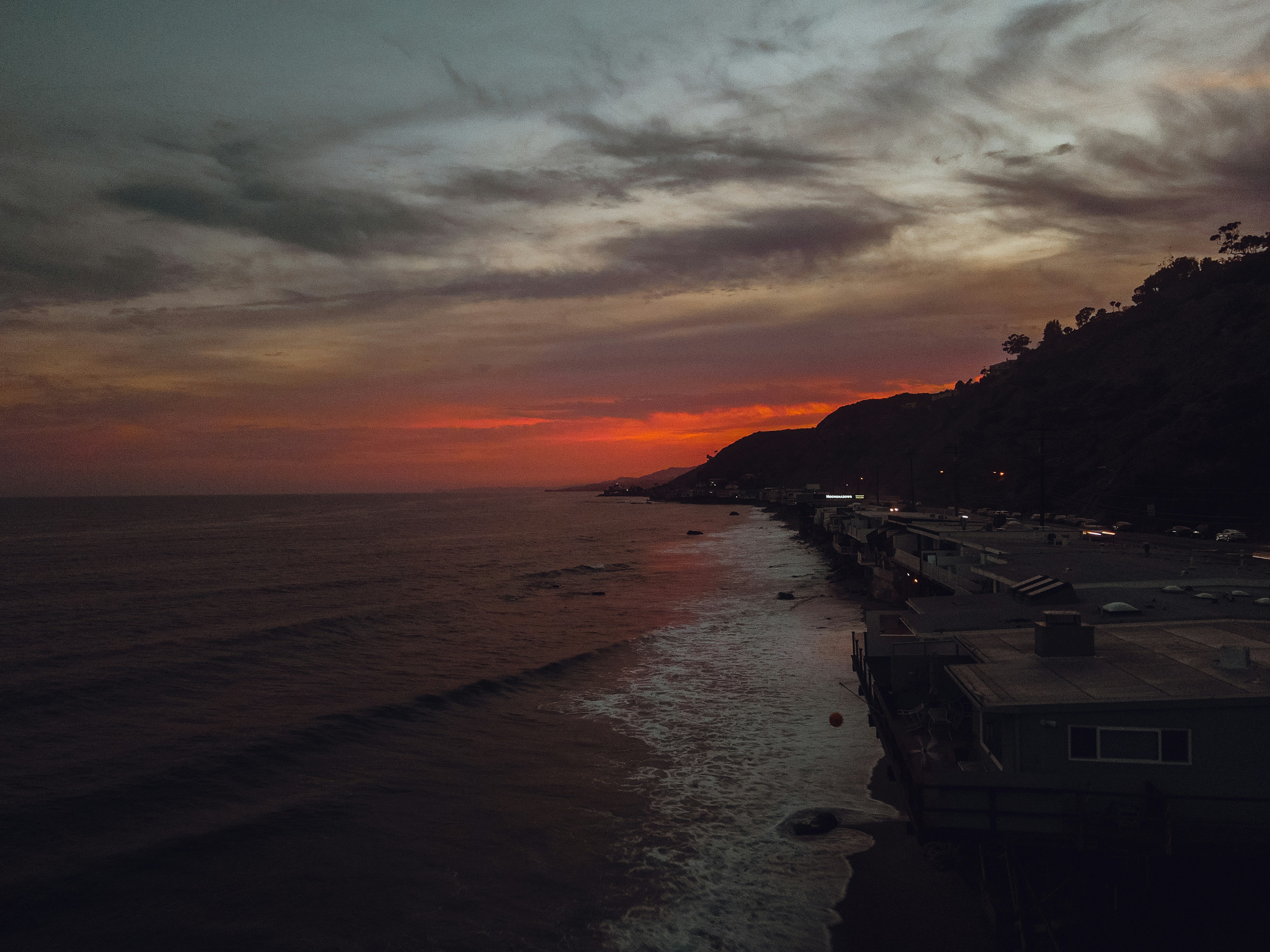 a sunset view of a beach with houses on the shore