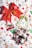 A collection of Christmas-themed decorations placed on a festive fabric featuring snowmen and reindeer patterns. The central items include a large red bow with snowflake and holly designs, a small decorative red car with a Christmas tree on top, a green and white Christmas tree ornament, and a handmade reindeer ornament within a rustic wreath. The background fabric enhances the holiday theme with illustrations like candy canes and Santa hats.