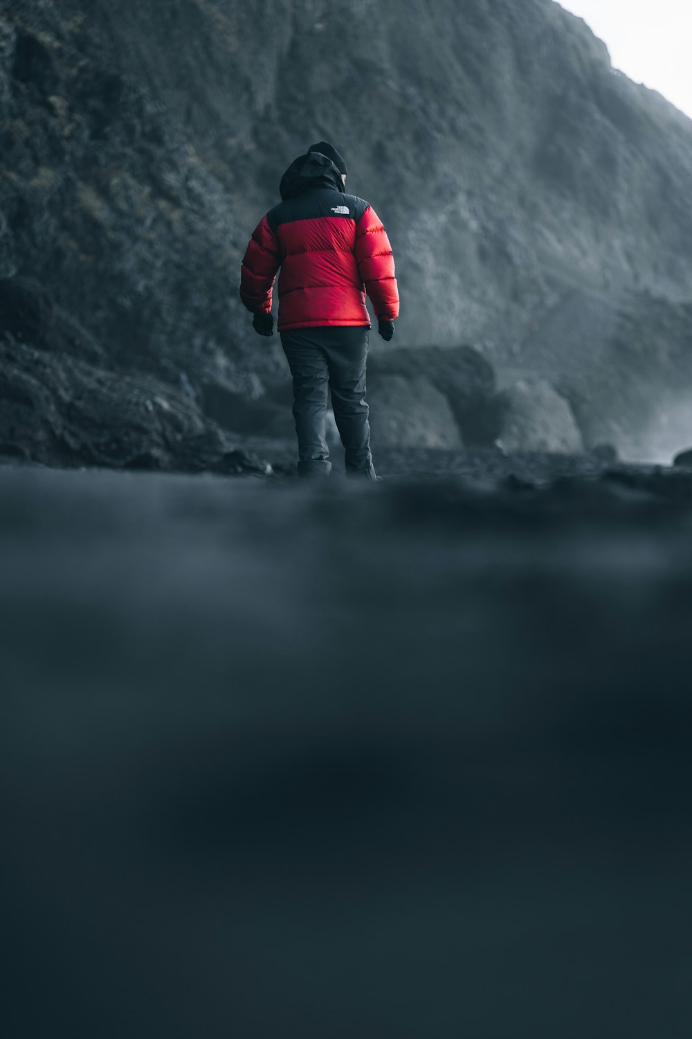 a person in a red jacket standing on a rocky beach