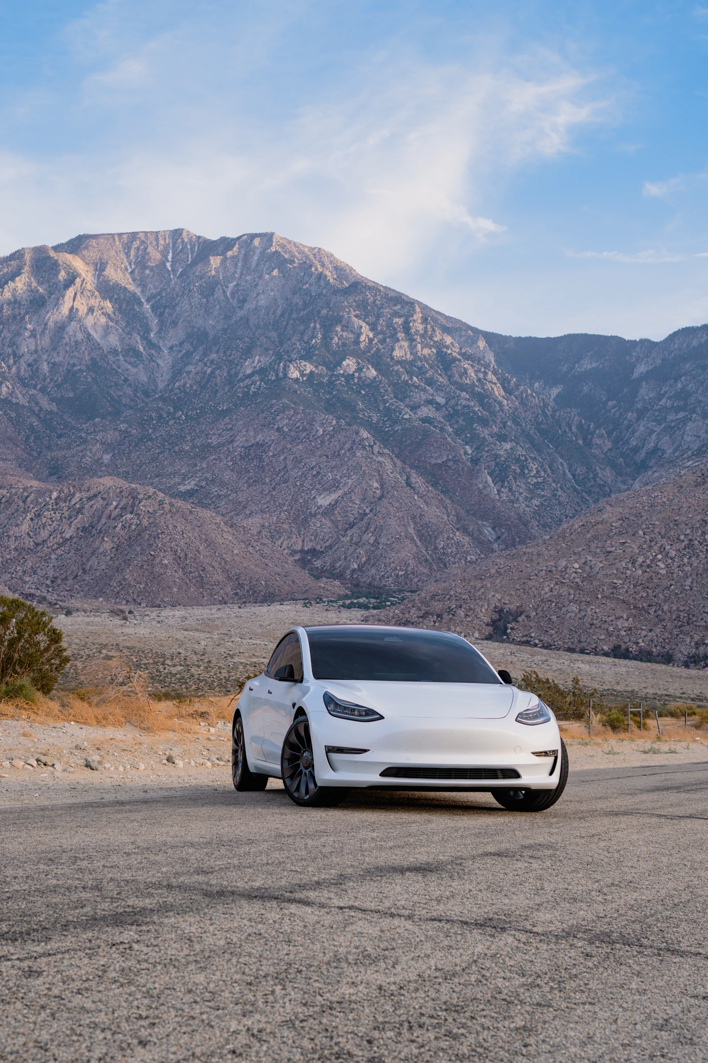 A white Tesla parked below a bright mountain ridge