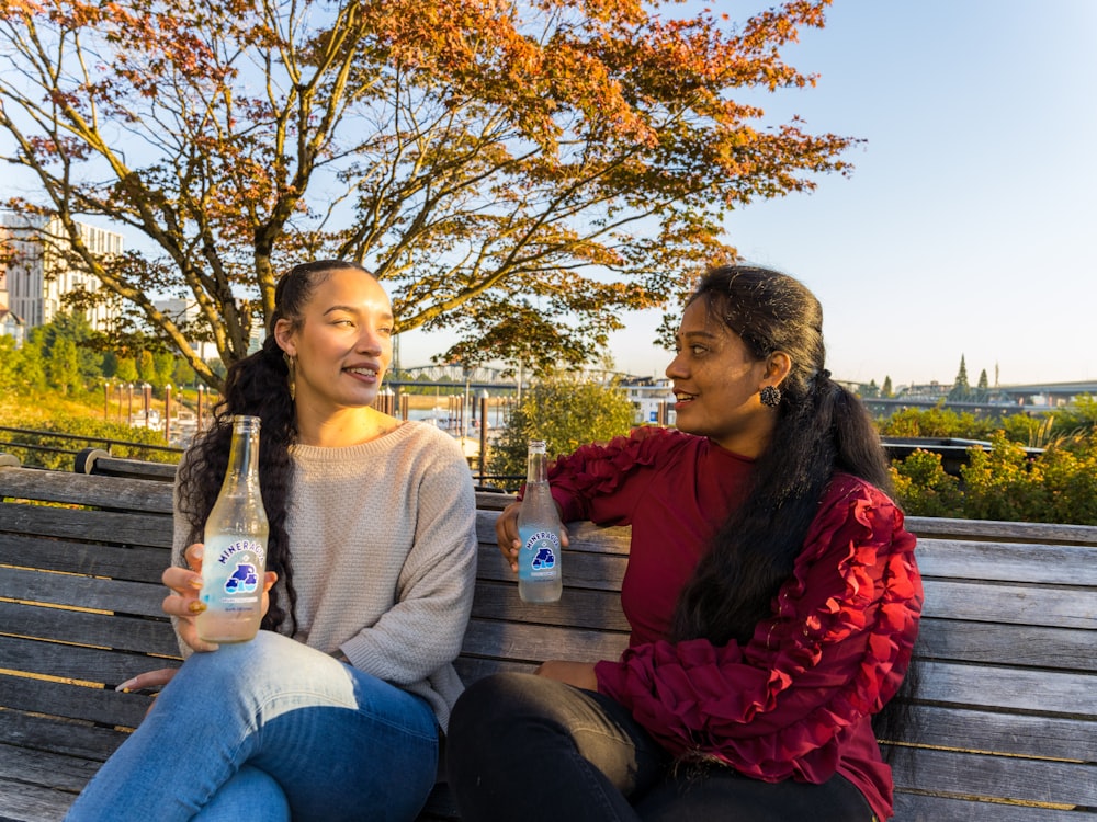 two women sitting on a bench with drinks