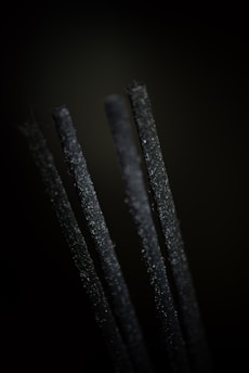 Four upright black incense sticks are in close-up focus against a dark background, emphasizing their textured surfaces.