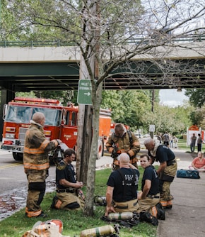 a group of firemen sitting on the ground next to a tree
