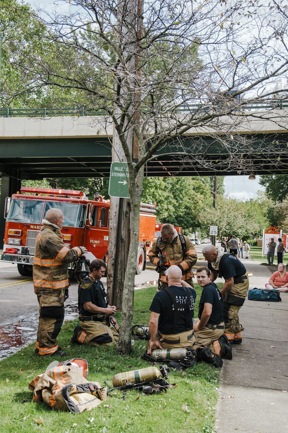 a group of firemen sitting on the ground next to a tree