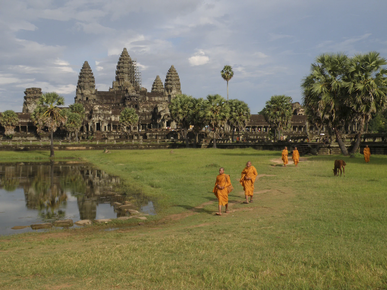 Angkor Wat in daylight, monks crossing the grass in front of the temple