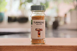 Close-up of a jar of golden ghee surrounded by fresh ingredients like turmeric and herbs on a rustic wooden table.