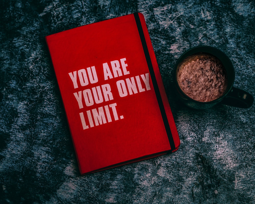 a red book with the words you are your only limit next to a cup of