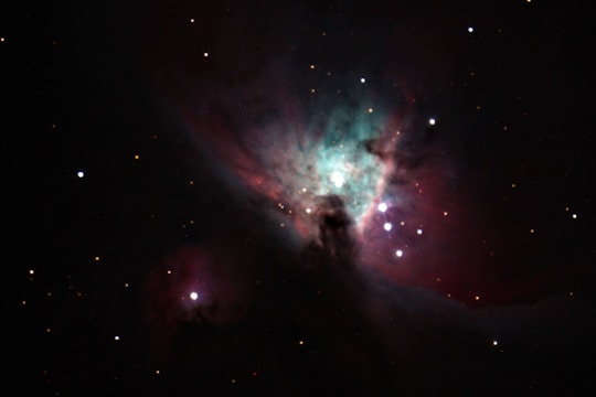 A vibrant nebula with bright stars scattered throughout the cosmic cloud. The nebula showcases a mix of teal and pink hues, creating a captivating and ethereal celestial scene.