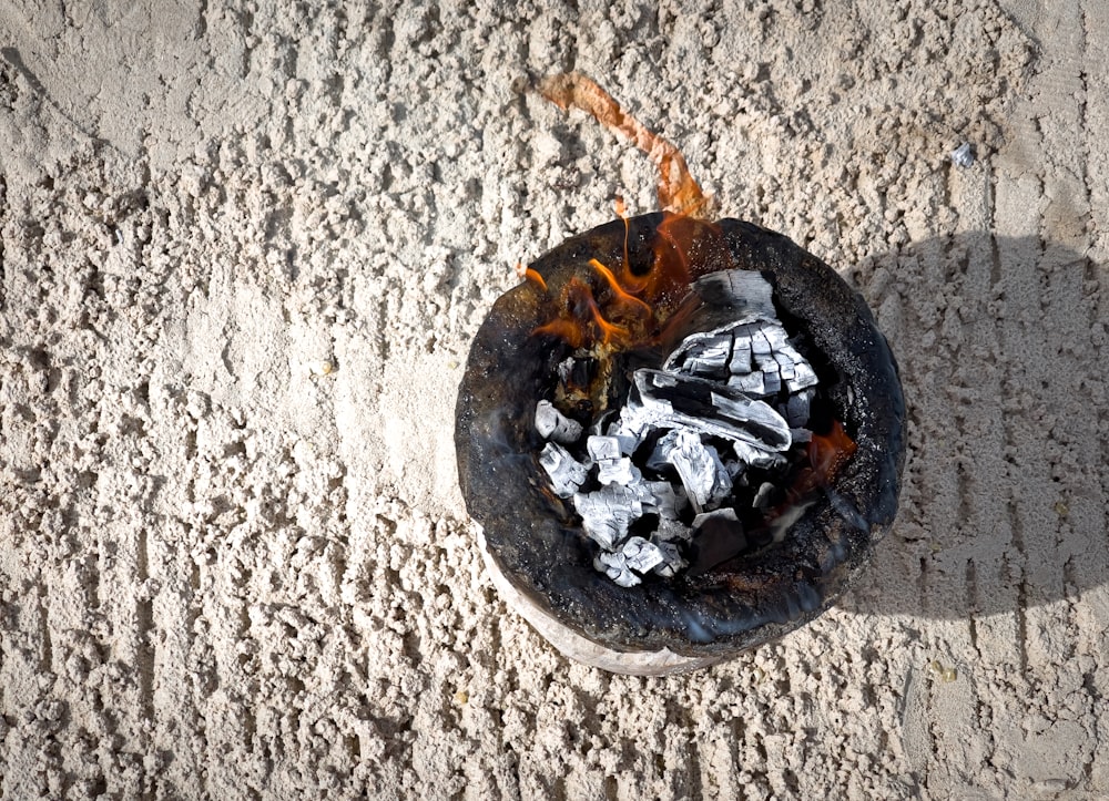 a bowl filled with coal sitting on top of a sandy beach