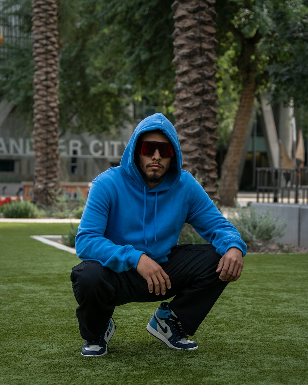 a man in a blue hoodie squatting on the grass