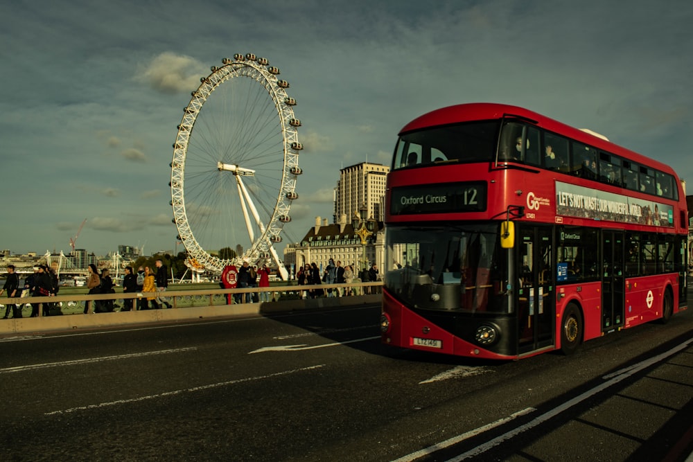 a red double decker bus driving past a ferris wheel