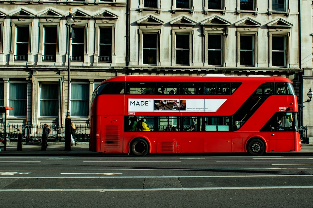 a red double decker bus driving past a tall building