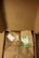 A cardboard box opened to reveal brown paper wrapping tied with twine. There is an eco-friendly label, a small card, and an envelope on top of the wrapping. The inside lid has a small pattern printed on it.