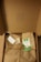 A cardboard box opened to reveal brown paper wrapping tied with twine. There is an eco-friendly label, a small card, and an envelope on top of the wrapping. The inside lid has a small pattern printed on it.