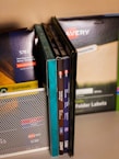 A collection of office supplies neatly arranged, including Avery label and card packages. The items are stored on a shelf and organized upright against a mesh divider. Various colors and sizes of packaging are visible, with text such as 'EcoFriendly' and product numbers.