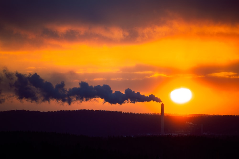 the sun is setting behind a factory with smoke coming out of it