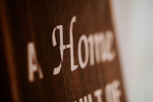 Blurry close-up of text on a brown surface with white lettering. The text reads 'A Home' with additional, partially obscured words.