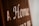 Blurry close-up of text on a brown surface with white lettering. The text reads 'A Home' with additional, partially obscured words.