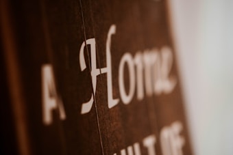 Blurry close-up of text on a brown surface with white lettering. The text reads 'A Home' with additional, partially obscured words.