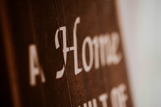 Blurry close-up of text on a brown surface with white lettering. The text reads 'A Home' with additional, partially obscured words.