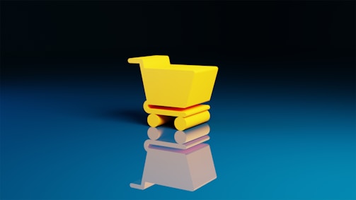 A small, bright yellow shopping cart sits on a reflective blue surface, creating a mirror effect. The background is a gradient from deep black at the top to a lighter blue at the bottom.