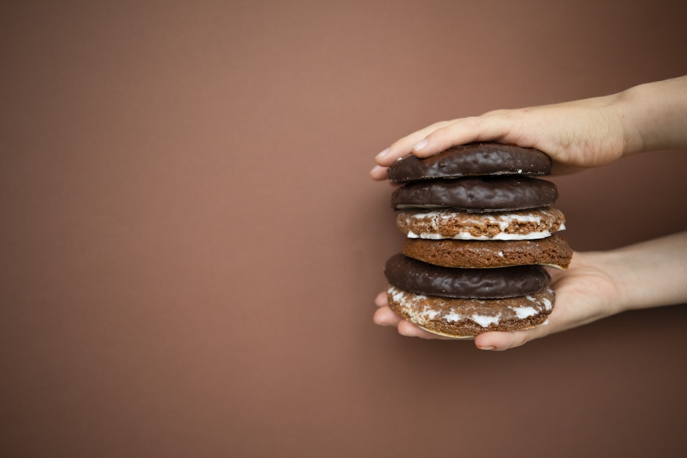 a person holding a stack of chocolate covered donuts