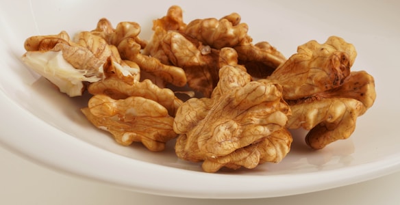 A collection of walnut halves with intricate textures and brown hues placed on a white plate. The surface of the plate is smooth and glossy, providing contrast to the rough surface of the walnuts.