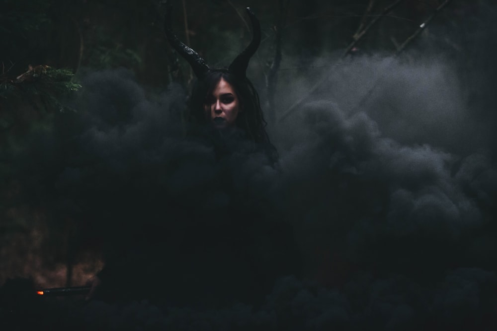 a woman with long hair and horns standing in smoke