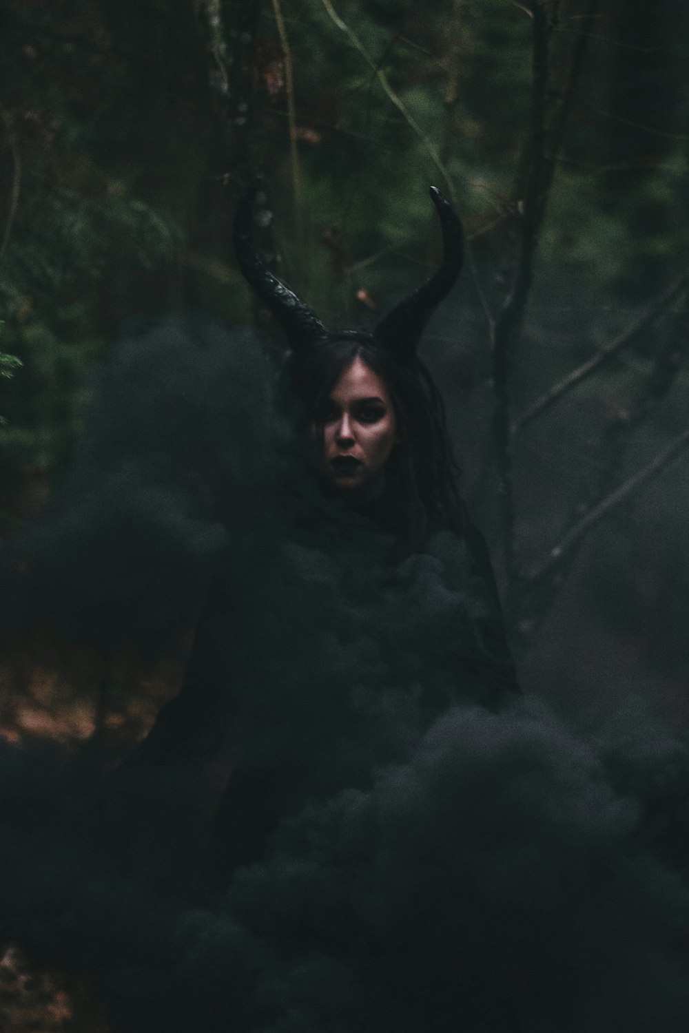 a woman with horns and black smoke in the woods
