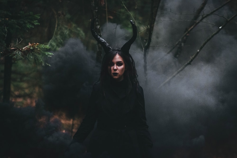 a woman with horns and horns standing in a forest
