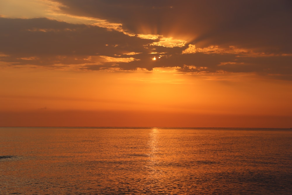 the sun is setting over the ocean with a boat in the water