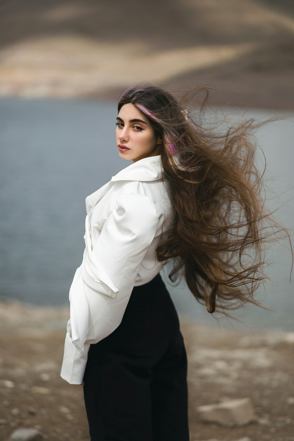 a woman with long hair standing near a body of water