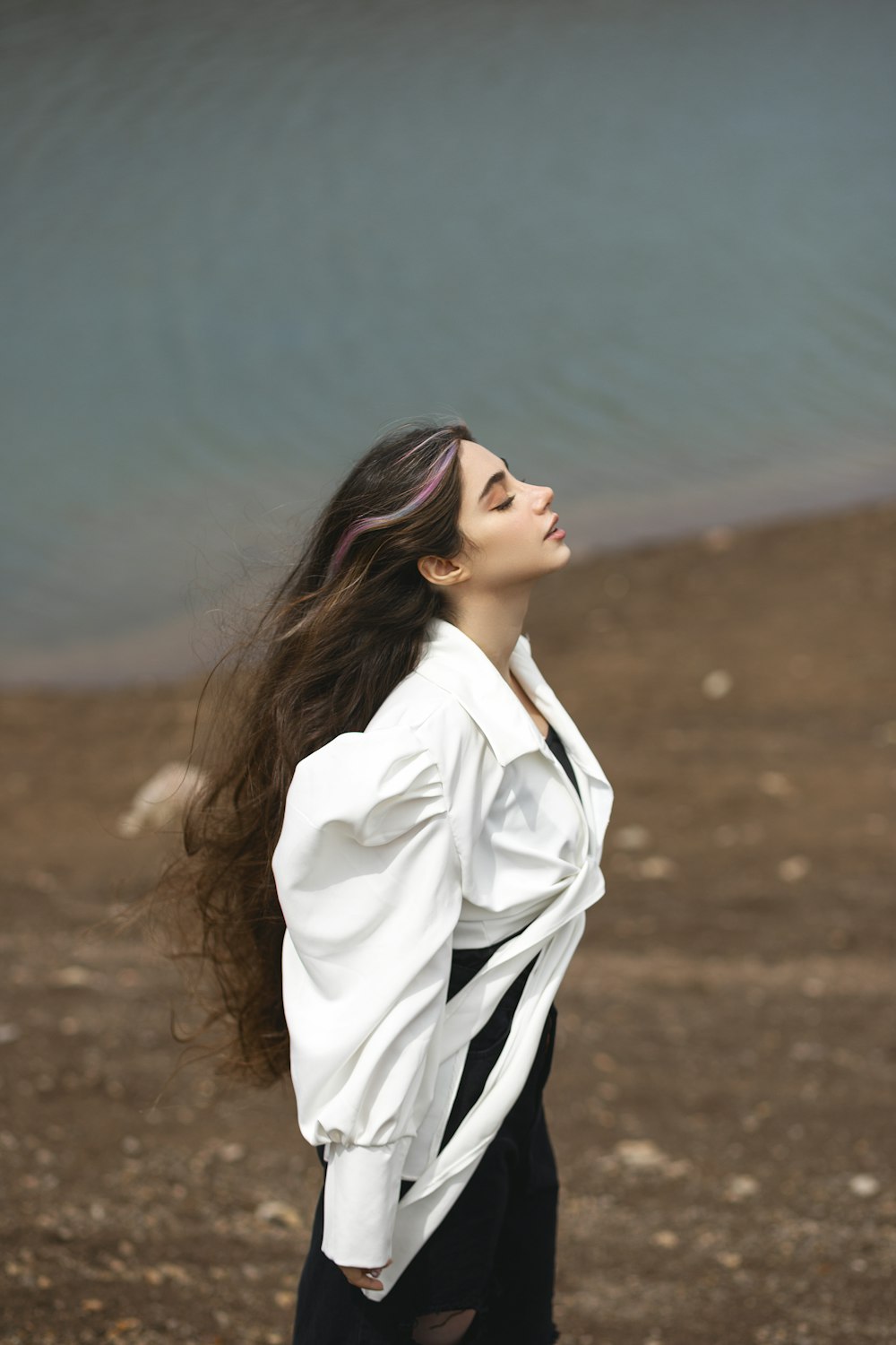 a woman with long hair standing near a body of water