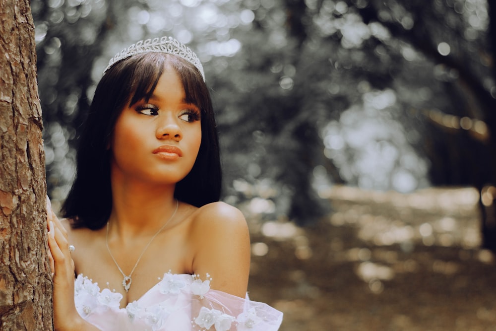 a woman wearing a tiara leaning against a tree