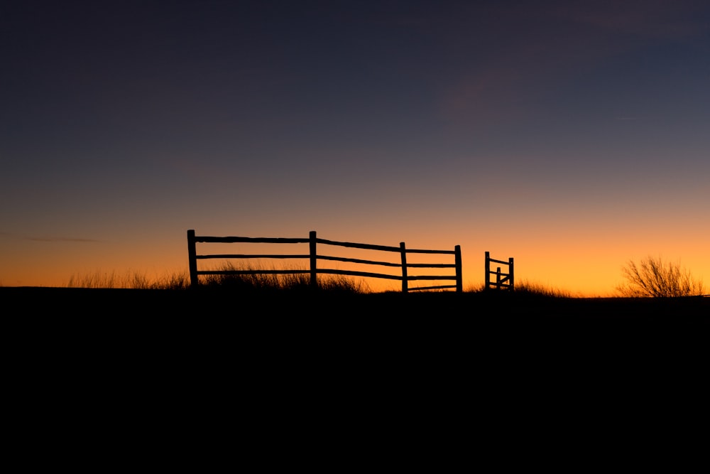 uma cerca de madeira em um campo ao pôr do sol