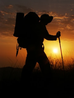 Sunset view of a lone hiker silhouetted against the sky, with an Amsonyns LLC backpack clearly visible