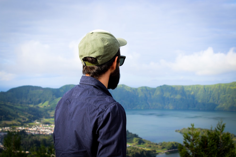 a man with a hat and sunglasses looking at a lake