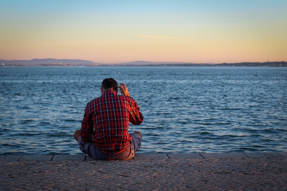 a man sitting on the edge of a pier taking a picture of the water