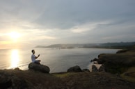 A peaceful scene of a woman meditating on a cliff overlooking the ocean at sunset.