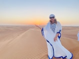 A flowing North African kaftan displayed against a backdrop of desert dunes at sunset.